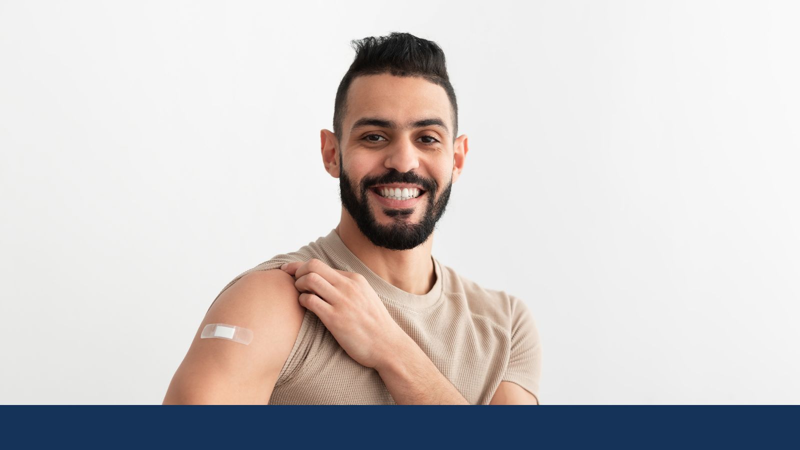 A man with black hair and beard pulls up his sleeve to show a Band-Aid on his arm.