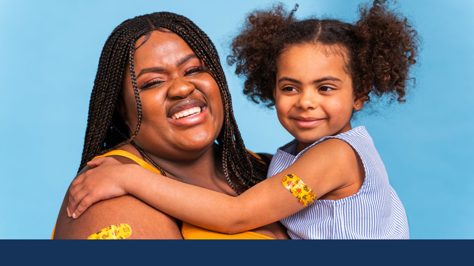 A woman with braids holds a young child. Both have yellow Band-Aids.